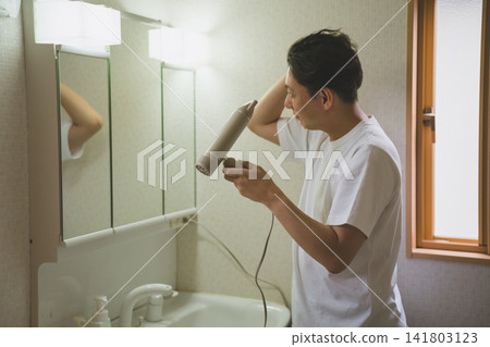 A man in his 40s using a hairdryer in the bathroom. A man in his 40s using a hairdryer in the bathroom. 141803123