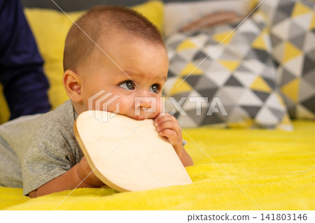 Infant Biting Wooden Activity Board On Yellow Blanket Infant Biting Wooden Activity Board On Yellow Blanket 141803146