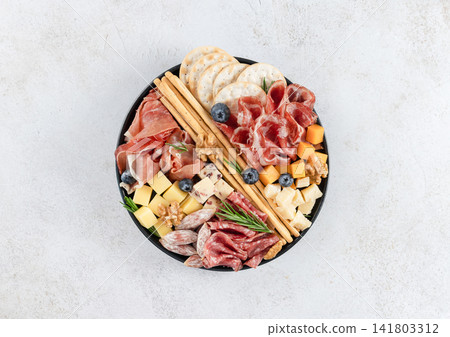 Charcuterie board cured meats, cheeses, crackers, breadsticks, walnuts on white background. Top view Charcuterie board cured meats, cheeses, crackers, breadsticks, walnuts on white background. Top view 141803312