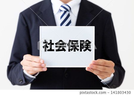 A young businessman in a business suit holding a whiteboard with information about social insurance. A young businessman in a business suit holding a whiteboard with information about social insurance. 141803430