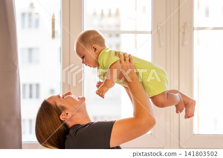 Baby Boy Touches Mother Chin During Playful Window Moment 141803502
