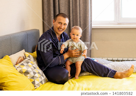 Smiling Father Holding Baby Son On Bed At Home Smiling Father Holding Baby Son On Bed At Home 141803582
