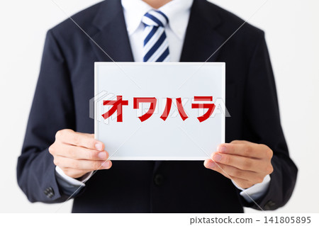 A young businessman in a business suit holding a whiteboard with the words "Owahara" (job-hunting harassment) on it. 141805895