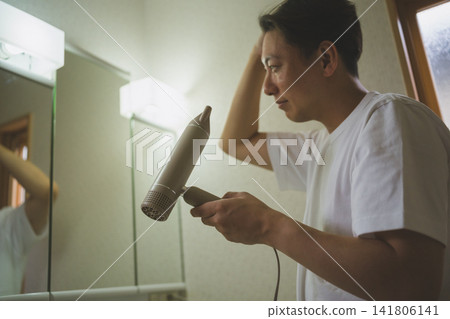 一位四十多歲的男子正在用吹風機吹頭髮。 141806141