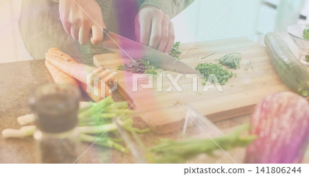 Chopping home cook wearing olive jacket cutting chives on wood board at kitchen counter, with knife Chopping home cook wearing olive jacket cutting chives on wood board at kitchen counter, with knife 141806244