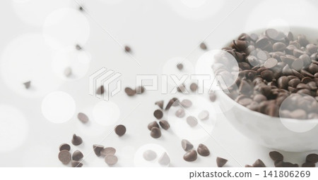 Displaying white ceramic bowl overflowing dark chocolate chips on countertop, bokeh, copy space Displaying white ceramic bowl overflowing dark chocolate chips on countertop, bokeh, copy space 141806269