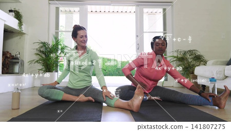 Stretching two women wearing pink and green tops on black mats in living room, math overlays Stretching two women wearing pink and green tops on black mats in living room, math overlays 141807275
