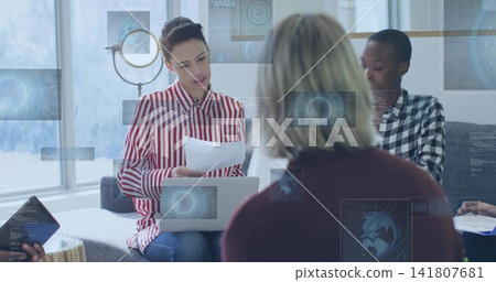 Leading woman in red-striped shirt reading pages and holding laptop in office lounge, tablet, HUD 141807681
