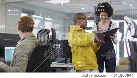 Reviewing tablet, man in yellow hoodie alongside woman gesturing at open office with AR overlays Reviewing tablet, man in yellow hoodie alongside woman gesturing at open office with AR overlays 141807944