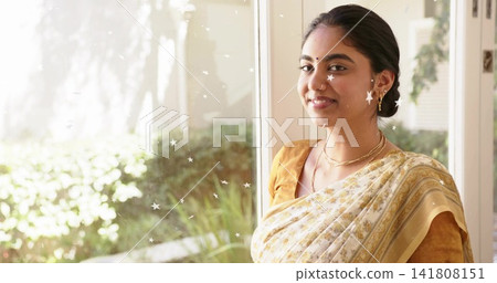 Standing Indian woman wearing gold saree by starred glass window, bindi, copy space 141808151