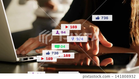 Tapping woman wearing black long-sleeve top using laptop and tablet at table with social overlays Tapping woman wearing black long-sleeve top using laptop and tablet at table with social overlays 141808932