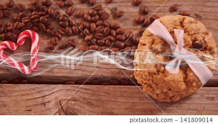 Showing oatmeal cookie tied with bow on rustic tabletop, coffee beans, candy cane heart, copy space Showing oatmeal cookie tied with bow on rustic tabletop, coffee beans, candy cane heart, copy space 141809014