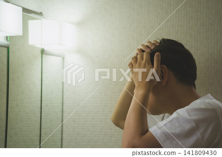 一位四十多歲的男子,因頭髮稀疏而苦惱,在浴室鏡子前雙手抱頭。 一位四十多歲的男子,因頭髮稀疏而苦惱,在浴室鏡子前雙手抱頭。 141809430