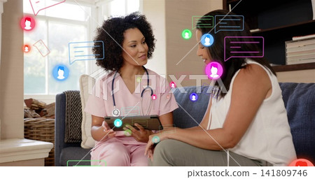 Showing clinician in pink scrubs with stethoscope using tablet on living room sofa, chat graphics Showing clinician in pink scrubs with stethoscope using tablet on living room sofa, chat graphics 141809746