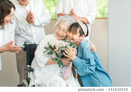 Smiling granddaughter presents a bouquet of flowers to her grandmother in a wheelchair Smiling granddaughter presents a bouquet of flowers to her grandmother in a wheelchair 141810533