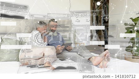 Holding tablet, mature couple leaning on bed at home, wearing casual clothes, digital overlay Holding tablet, mature couple leaning on bed at home, wearing casual clothes, digital overlay 141810712