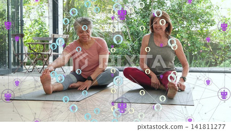Reaching toward foot two women on yoga-mats in home with glass-wall, pink-top grey-tank, overlay Reaching toward foot two women on yoga-mats in home with glass-wall, pink-top grey-tank, overlay 141811277