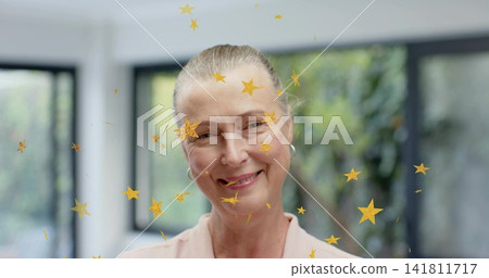 Smiling mature woman wearing pink blouse, hoop earrings, near black-framed windows with gold stars. Portrait, adult, serene, natural, light, bokeh, overlay 141811717