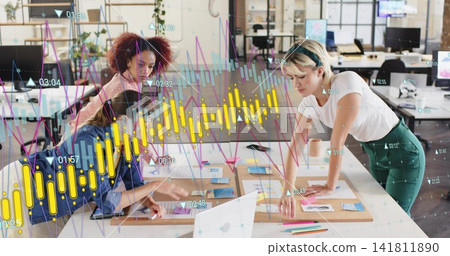 Leaning three women in casual attire pointing at wood table and sticky notes, showing data overlays 141811890