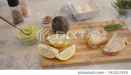 Preparing wooden cutting board with whole avocado, halved lemon, bread slices on marble countertop Preparing wooden cutting board with whole avocado, halved lemon, bread slices on marble countertop 141812426