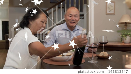 Reaching woman wearing white while man wearing blue holding wine bottle and glass at dining table Reaching woman wearing white while man wearing blue holding wine bottle and glass at dining table 141813347