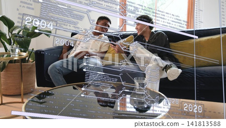 Showing two men in polo and sweatshirt sharing smartphone on sofa in living room, holographic UI Showing two men in polo and sweatshirt sharing smartphone on sofa in living room, holographic UI 141813588
