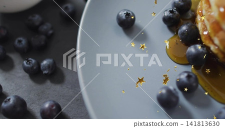Showing pancake stack dripping maple syrup on grey plate at dark slate, blueberries and gold stars Showing pancake stack dripping maple syrup on grey plate at dark slate, blueberries and gold stars 141813630