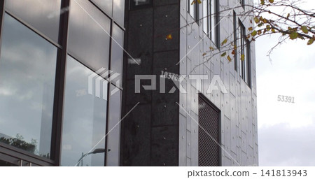 Showing facade on urban street with mirrored glass dark cladding light panels vent and faint digits Showing facade on urban street with mirrored glass dark cladding light panels vent and faint digits 141813943
