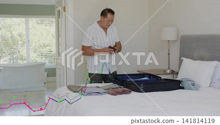 Packing mature Chinese man in striped shirt arranging open suitcase in bedroom, holding passport Packing mature Chinese man in striped shirt arranging open suitcase in bedroom, holding passport 141814119