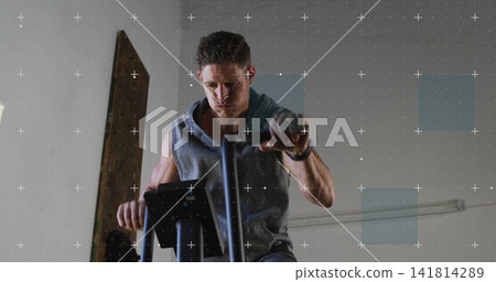 Pedaling man in sleeveless gray hoodie at gym on bike, gripping handlebars with watch and earbud Pedaling man in sleeveless gray hoodie at gym on bike, gripping handlebars with watch and earbud 141814289