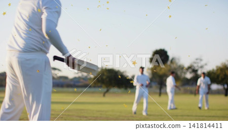 Holding wooden cricket bat, batsman wearing white kit at local park with gold confetti, copy space Holding wooden cricket bat, batsman wearing white kit at local park with gold confetti, copy space 141814411