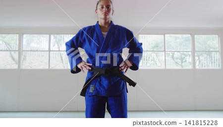 Standing female martial arts student holding focused stance in dojo, wearing blue gi and black belt Standing female martial arts student holding focused stance in dojo, wearing blue gi and black belt 141815228