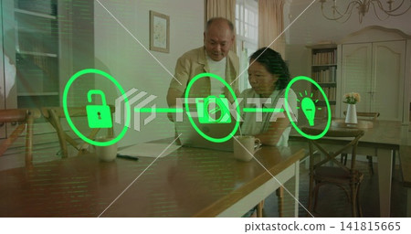 Reviewing senior couple wearing cardigans using laptop at dining area, with smart-home icons, mugs Reviewing senior couple wearing cardigans using laptop at dining area, with smart-home icons, mugs 141815665