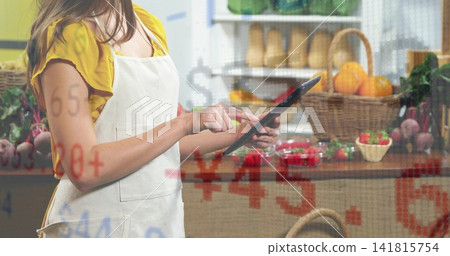 Using tablet vendor wearing yellow top and apron checking prices at stall, with price overlay 141815754