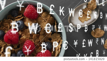 Showing blue bowl of bran cereal sitting left on slate table, with berries, spoon, currency symbols 141815820