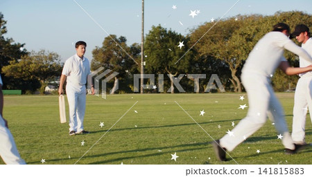 Standing batsman holding wooden bat left on field in white kit, teammates cheering, copy space Standing batsman holding wooden bat left on field in white kit, teammates cheering, copy space 141815883