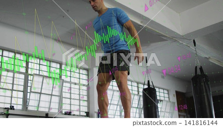 Balancing man wearing blue tee black-shorts on balance-board in gym, with bags and financial charts Balancing man wearing blue tee black-shorts on balance-board in gym, with bags and financial charts 141816144