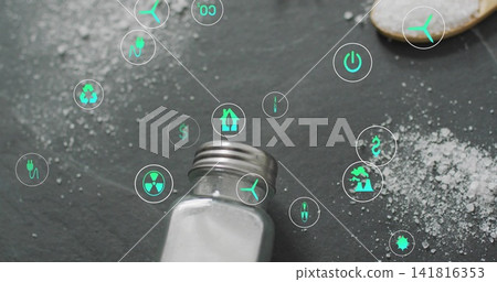 Showing metal-capped glass shaker spilling salt on dark slate, wooden spoon and green icons Showing metal-capped glass shaker spilling salt on dark slate, wooden spoon and green icons 141816353