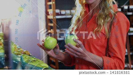 Choosing woman in orange-red shirt selecting fruit at grocery produce bin, holding two green apples Choosing woman in orange-red shirt selecting fruit at grocery produce bin, holding two green apples 141816381