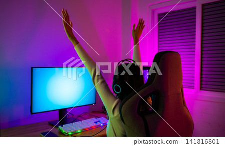 Winning Victory. Asian gamer playing online video game excited on desktop computer PC colorful neon LED lights, young woman in gaming headphones using computer she happy successful Winning Victory. Asian gamer playing online video game excited on desktop computer PC colorful neon LED lights, young woman in gaming headphones using computer she happy successful 141816801