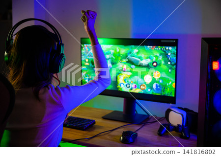 Winning. Young woman in gaming headphones playing video game online at home neon room feel excited, Happy Gamer young plays online video games computer she raises hands to wins tournament Winning. Young woman in gaming headphones playing video game online at home neon room feel excited, Happy Gamer young plays online video games computer she raises hands to wins tournament 141816802