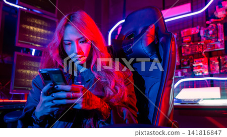 Asian woman in front of a computer monitor display using mobile phone, neon light, Hacker wear black jacket at system control room, Security guard working on multiple monitors together Asian woman in front of a computer monitor display using mobile phone, neon light, Hacker wear black jacket at system control room, Security guard working on multiple monitors together 141816847