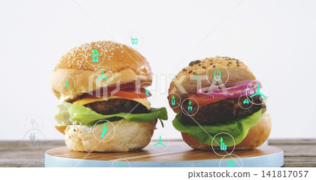 Showing two gourmet burgers sitting on round wooden board at tabletop, with teal energy icons Showing two gourmet burgers sitting on round wooden board at tabletop, with teal energy icons 141817057