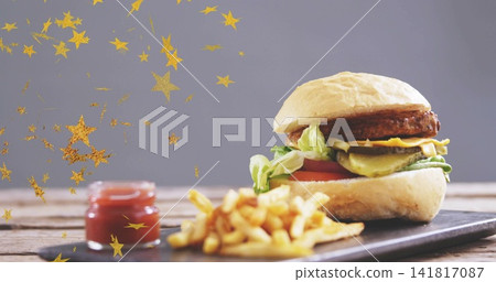 Showing assembled burger on slate board at table with fries ketchup gold star confetti, copy space Showing assembled burger on slate board at table with fries ketchup gold star confetti, copy space 141817087