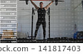 Lifting male wearing black tank, black leggings, pressing bar above in gym rack with market overlay 141817403