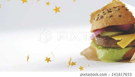 Showing seeded bun burger on right tabletop with patty, lettuce, pickles, gold stars, copy space Showing seeded bun burger on right tabletop with patty, lettuce, pickles, gold stars, copy space 141817653
