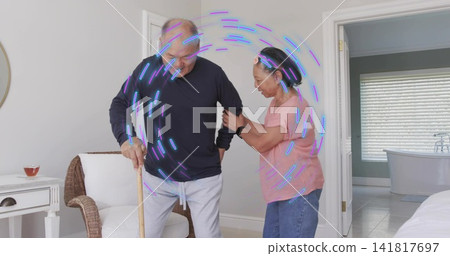 Senior woman supporting partner using wooden cane in bedroom, wearing pink top, jeans, smartwatch Senior woman supporting partner using wooden cane in bedroom, wearing pink top, jeans, smartwatch 141817697