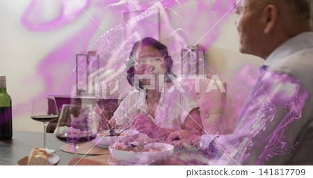 Gesturing senior woman in light blouse at dining table, man listening with wine and purple swirl Gesturing senior woman in light blouse at dining table, man listening with wine and purple swirl 141817709