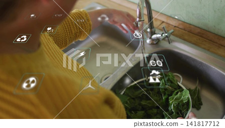 Rinsing greens, woman wearing mustard sweater holding metal bowl under faucet at home sink with AR Rinsing greens, woman wearing mustard sweater holding metal bowl under faucet at home sink with AR 141817712