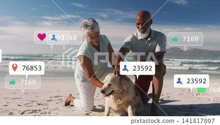 Kneeling mature couple petting golden retriever on beach with casual beachwear and social overlays 141817807